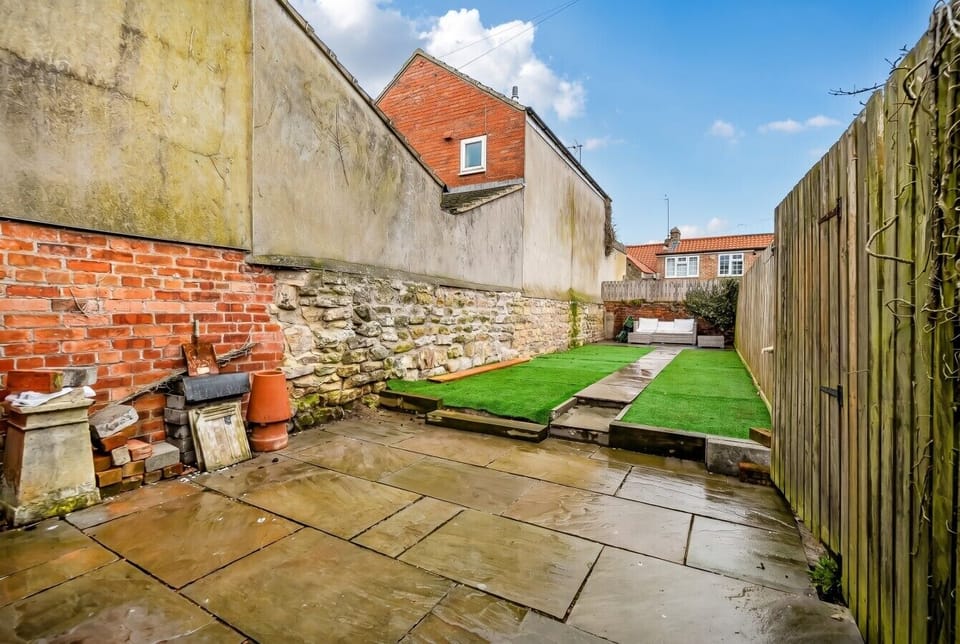 Private enclosed garden blending paved patio with a neat lawn area.