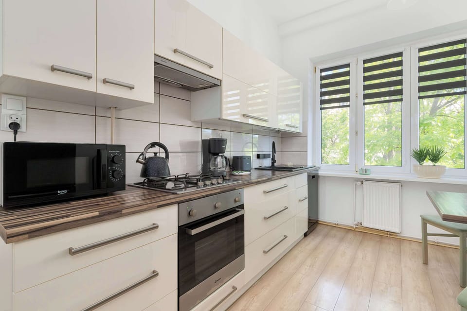 A modern kitchen includes white cabinets, built-in appliances, and long countertops beneath wide windows. Natural daylight brightens the cooking area.