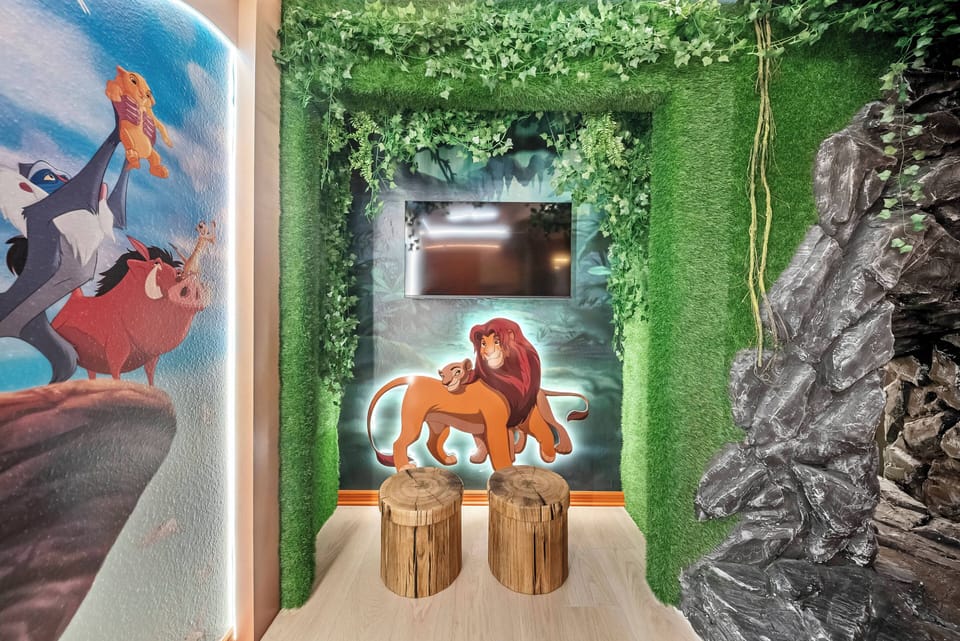 Discover a charming spot adorned with vibrant murals celebrating classic animation, surrounded by lush greenery. Cozy wooden stools enhance the playful atmosphere, creating the perfect place for your family to relax and enjoy.