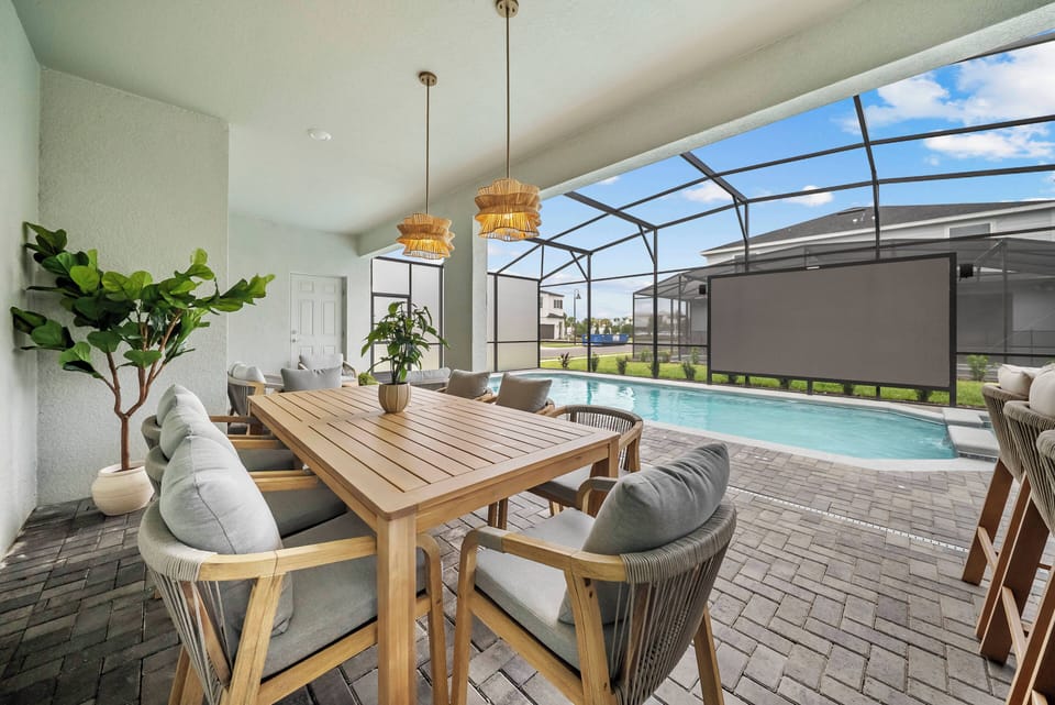 Experience a bright, airy dining area with a spacious wooden table and cushioned chairs. Enjoy views of the inviting pool through large windows, complemented by stylish pendant lights that enhance the modern decor.