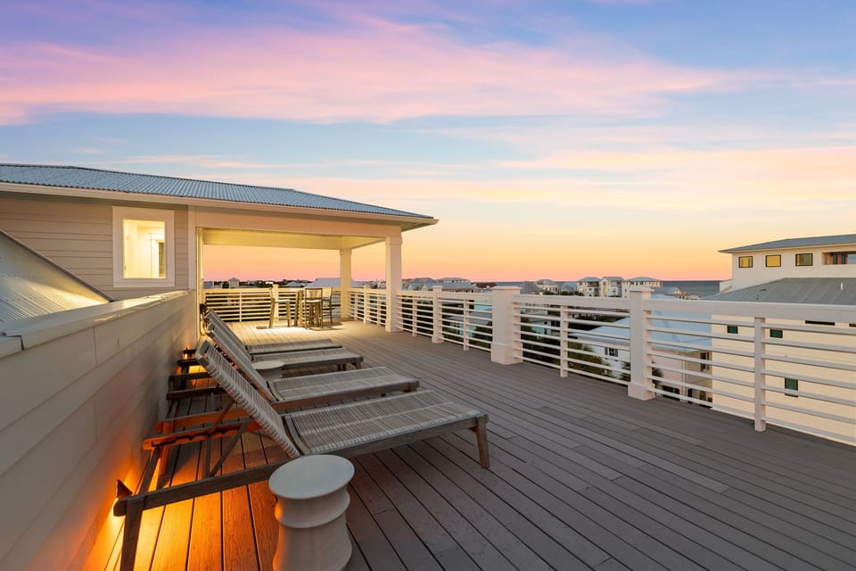 A rooftop deck offering sweeping views across a coastal neighborhood, with loungers positioned to capture pastel sunsets over rooftops and distant waters.