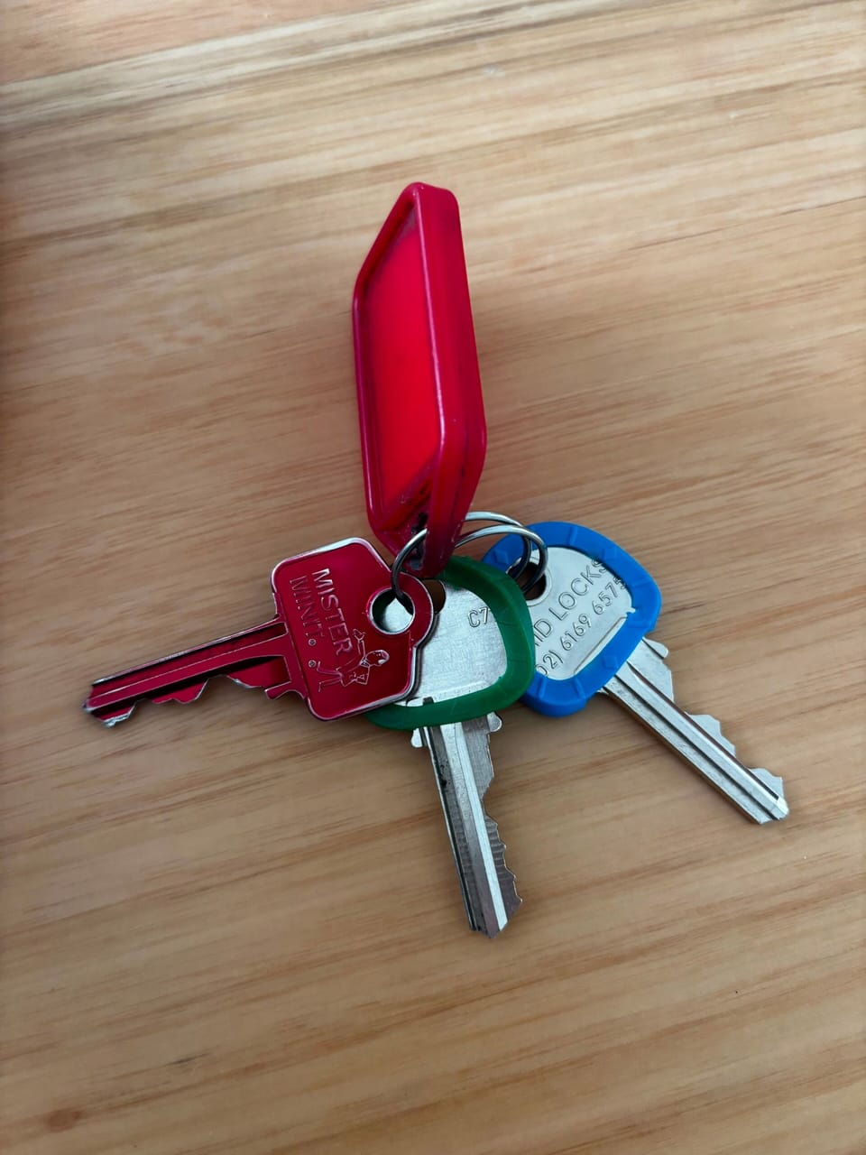 Easily access your home with this set of house keys, featuring colorful plastic key covers attached to a bright red fob on a wooden surface.