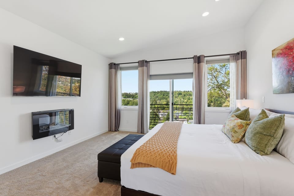 Bright modern bedroom with treetop views, TV, and sleek fireplace
