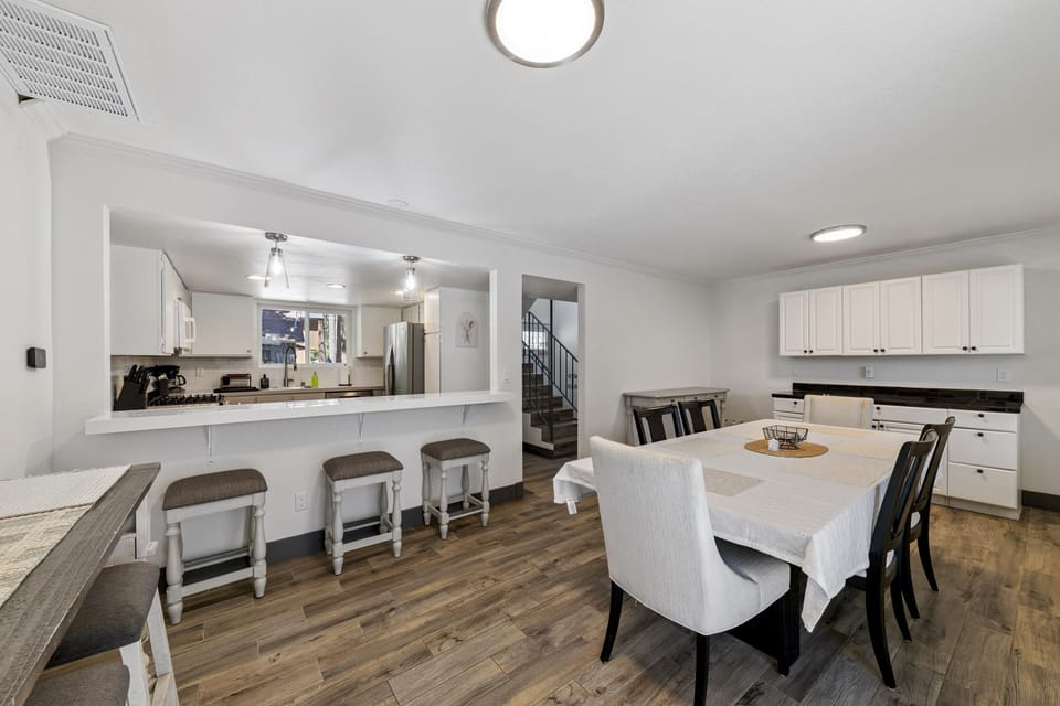 Dining room with a white tablecloth-covered table, six chairs, white cabinets, and wood-look flooring.