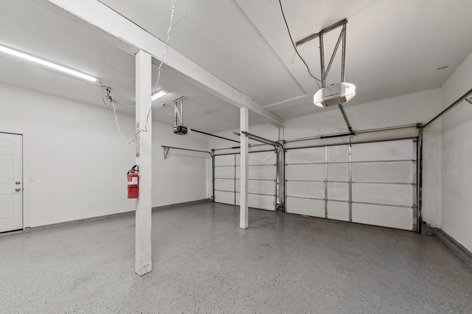Two-car garage with speckled gray floor, white walls, overhead fluorescent lighting, and automatic doors.