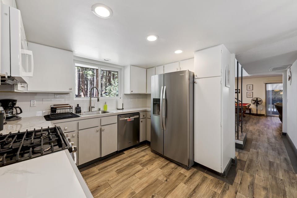 White cabinetry and stainless steel appliances line the kitchen with a window overlooking tall pine trees.