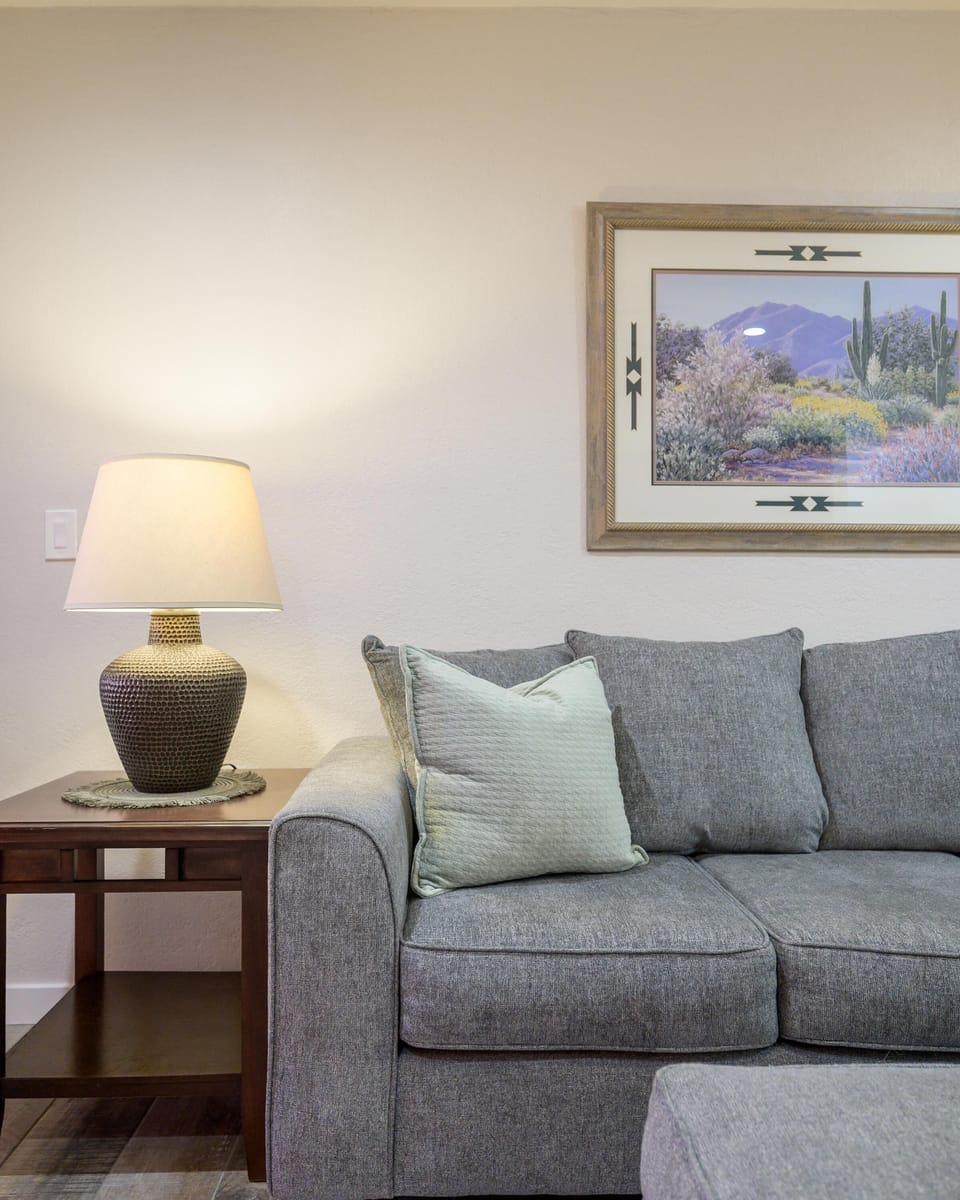 Dark wood side table holds textured ceramic lamp beside gray fabric sofa with pale green accent pillow.