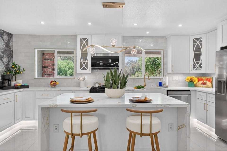 Gourmet chef`s kitchen featuring a massive quartz waterfall island with bar seating, custom gold-ribbon statement lighting, premium stainless steel appliances, under-cabinet lighting, and windows overlooking the mountains.
