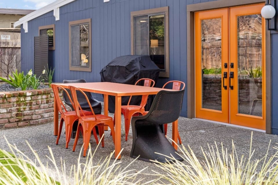 Outdoor dining.  Orange table and schoolhouse chairs with black Pantone chairs.  Barbecue gas grill for outdoor cooking. 