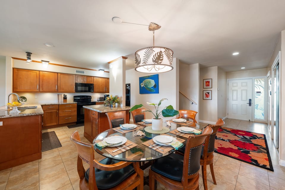 The formal dining space features a stylish glass table, matching chairs, and modern tropical light fixtures near the main entryway.