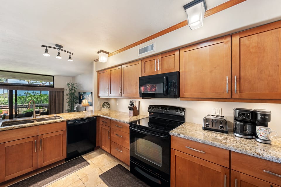 The modern kitchen is fully equipped with rich wood cabinetry, granite-style countertops, and full-size black and stainless steel appliances.