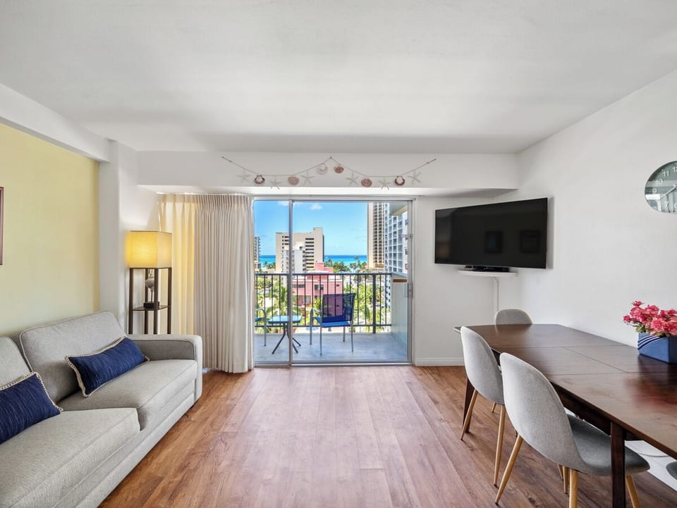 Living Area - Gather in a bright, easygoing living and dining space where the sofa, four-seat table, and open lanai/balcony share a partial Pacific view. It’s an inviting Waikiki home base for relaxing, dining, or working.