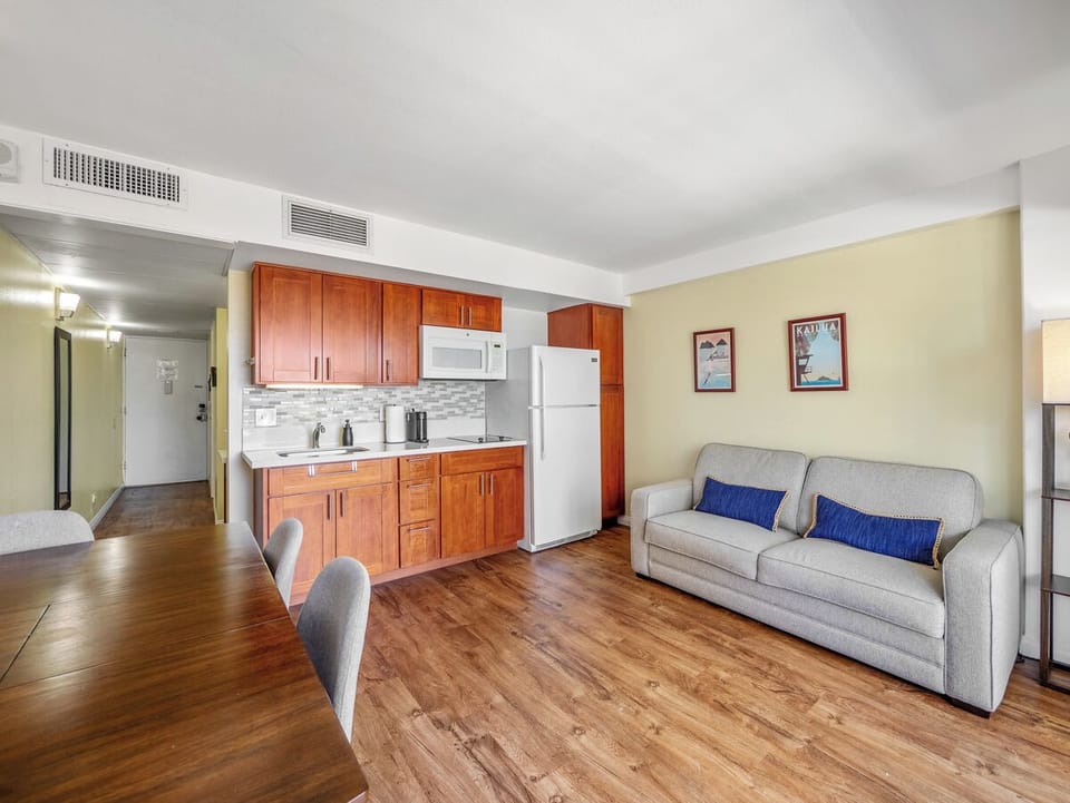 Living Area - Unpack and settle into a functional Waikiki home base with a queen sofa sleeper, dining and work surface, island artwork, and compact kitchen. Everything is arranged for comfortable routines during a month or longer.