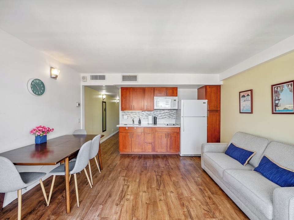 Living Area - Settle into an open living area designed for everyday comfort, with room to dine, work, lounge, and prepare simple meals. Warm wood finishes and blue accents add an easy island feel to this furnished Waikiki condo.