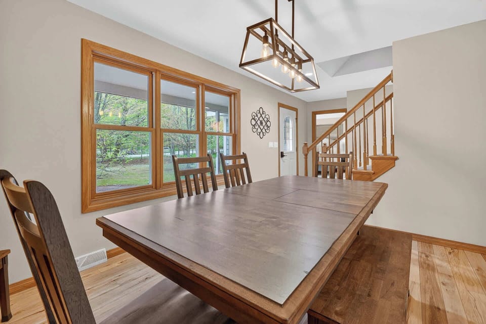 Gather around this inviting dining table, where natural light streams through beautiful windows and warm wood tones create the perfect setting for memorable meals together.
