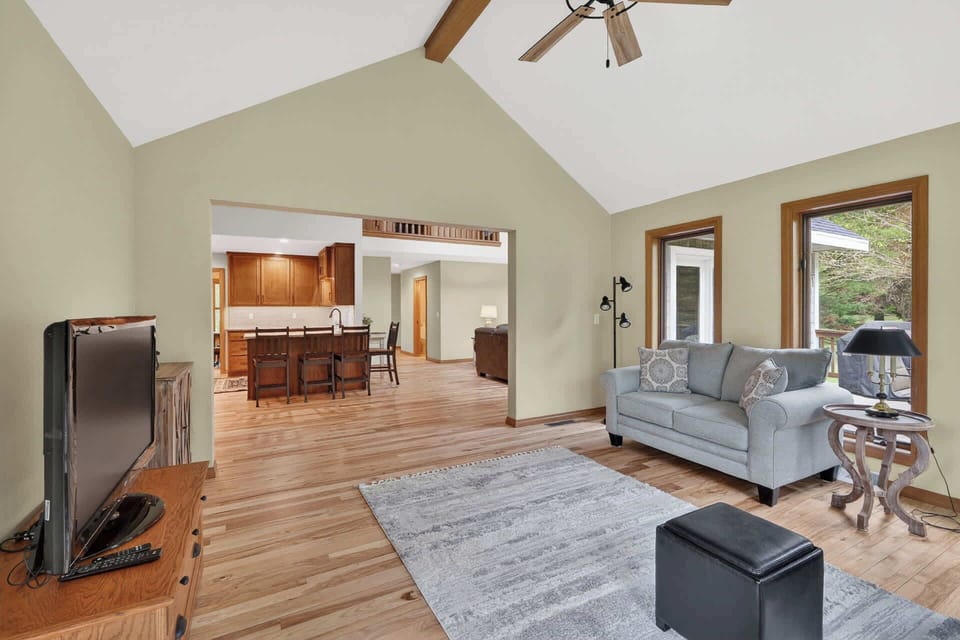 Relax in your bright, open living space with vaulted ceilings and warm wood accents. Large windows frame peaceful woodland views, while the open layout connects you seamlessly to the full kitchen and dining area.