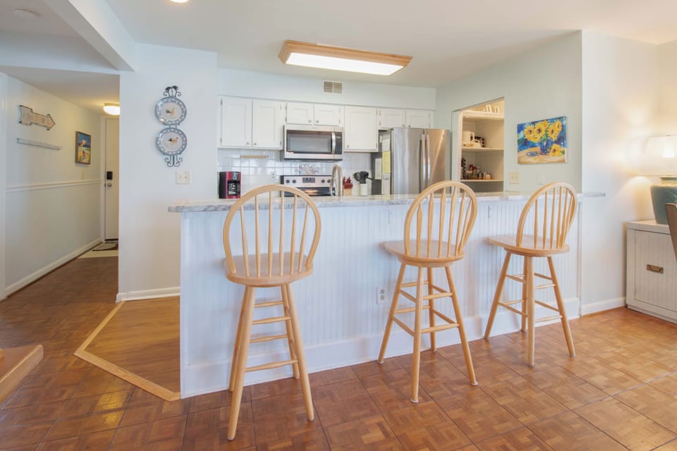 Cozy kitchen with white cabinetry and stainless steel appliances where you can enjoy morning coffee at the breakfast bar or whip up your favorite vacation meals.