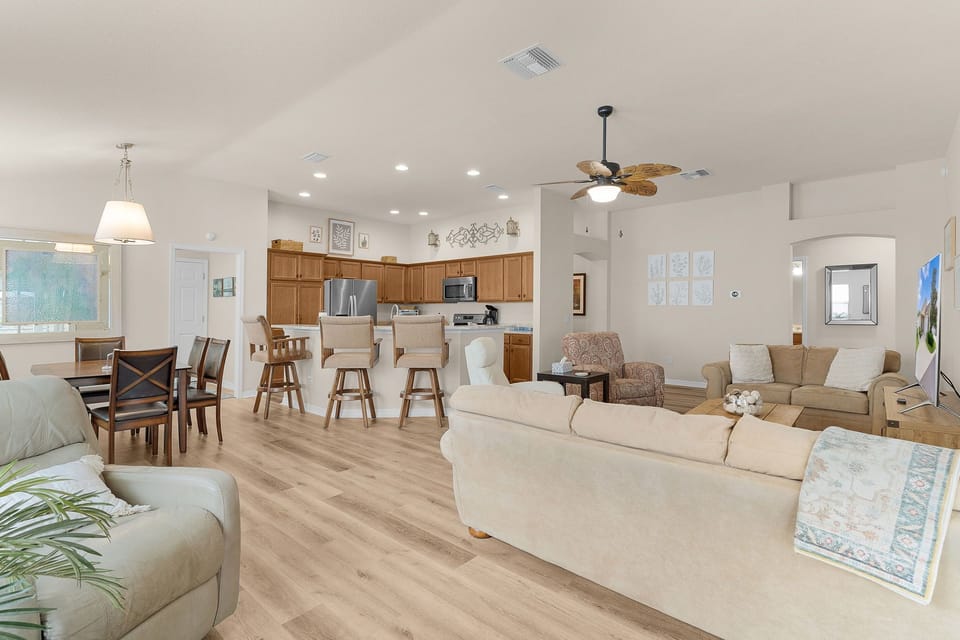 Settle into your open-concept retreat where natural light pours through, highlighting warm wood floors and comfortable furnishings. The fully-equipped kitchen invites you to prepare meals while staying connected to your group in the spacious living and din