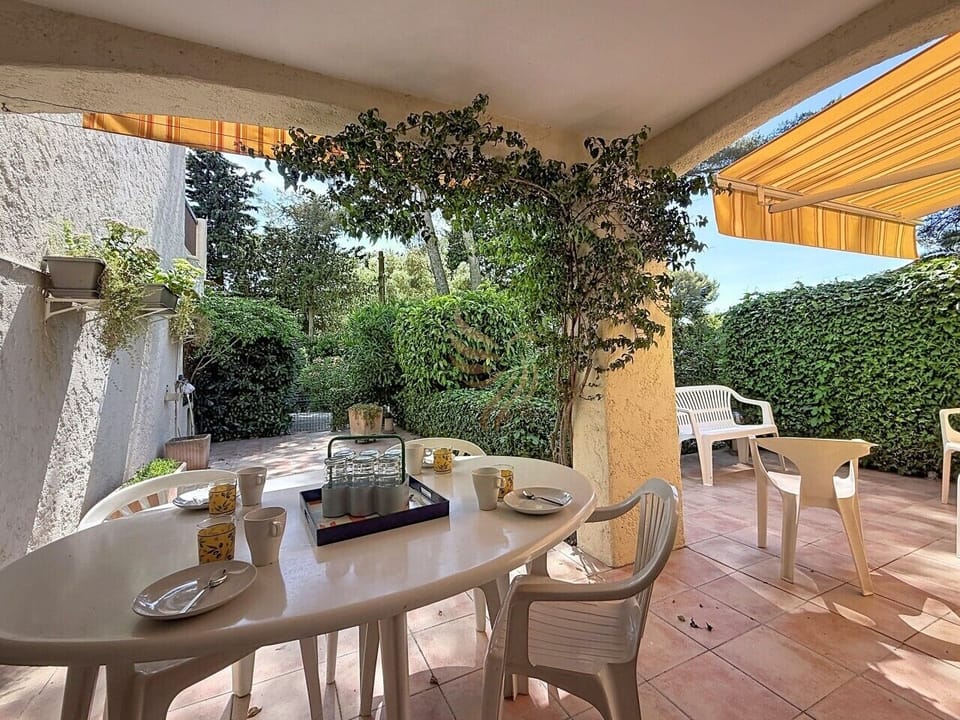 Petit-déjeuner paresseux sous le store rayé : la table dressée, les tasses jaunes et la vigne qui grimpe au pilier promettent une matinée douce et intime au cœur d’un jardin secret.