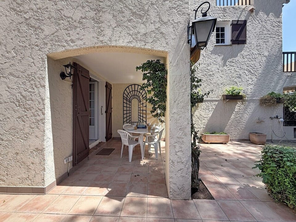 Installez-vous sous l`arche ombragée pour un petit-déjeuner au soleil : la table blanche, la vigne grimpante et la grille en fer racontent un après-midi provençal paisible, idéal pour se détendre à l`extérieur.