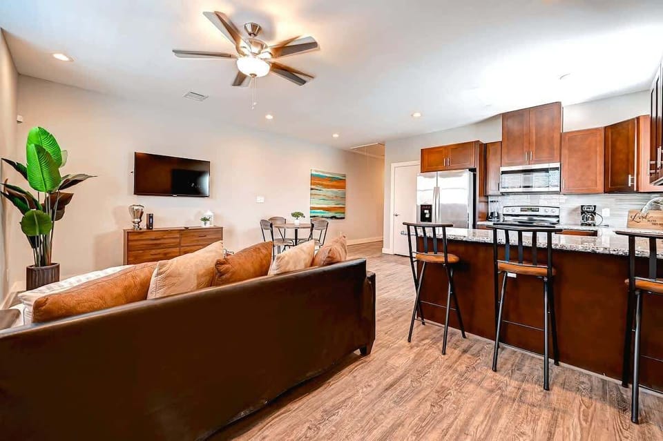 Inviting open-concept living area with a modern kitchen featuring granite countertops, stainless steel appliances, and a breakfast bar with seating. The cozy lounge space includes a TV,  a sofa, dining table, and stylish decor throughout.