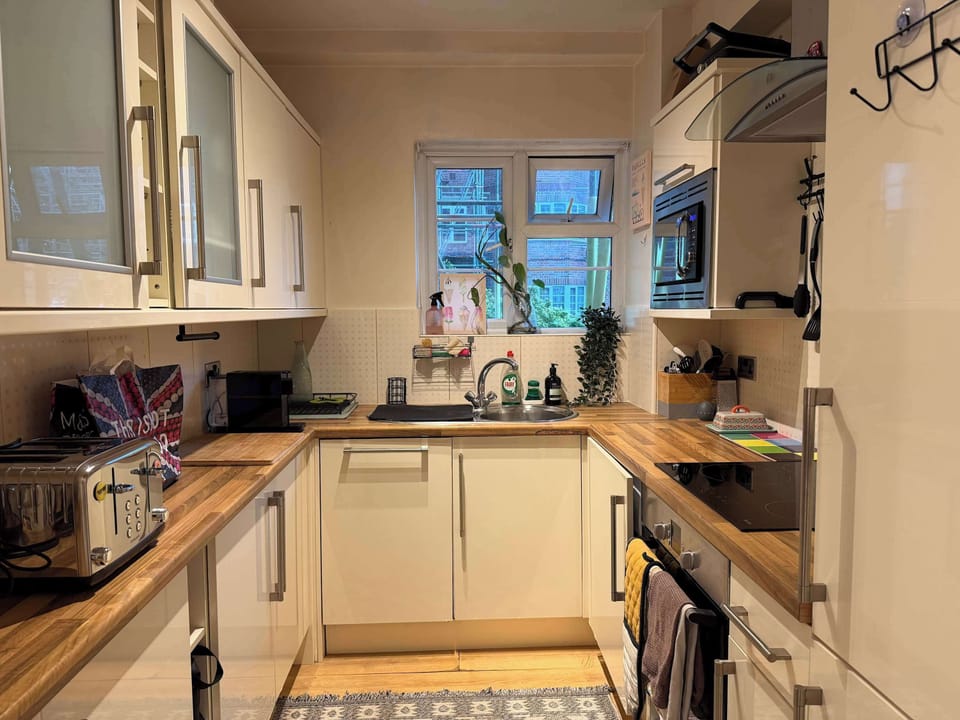 A small, modern kitchen features white cabinets, wooden countertops, and a window above the sink.