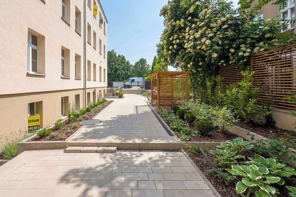 A landscaped courtyard path runs between residential buildings with greenery and trees along the sides. Outdoor space adds a peaceful setting.