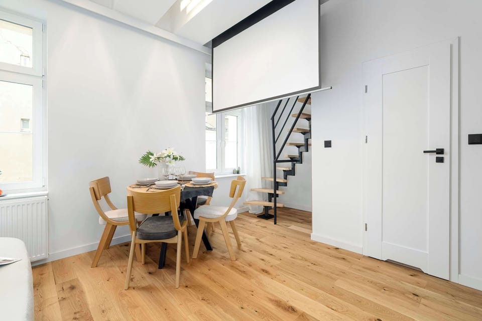 A dining area sits beside a staircase with black railings and white walls. The open-plan layout blends the living and dining zones.
