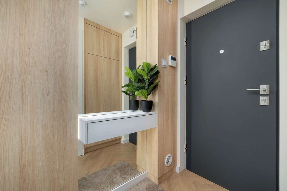 The entryway details a secure black front door equipped with a silver handle and an electronic peephole. Light wood wall panels frame the adjacent closet space, maintaining a cohesive interior style.