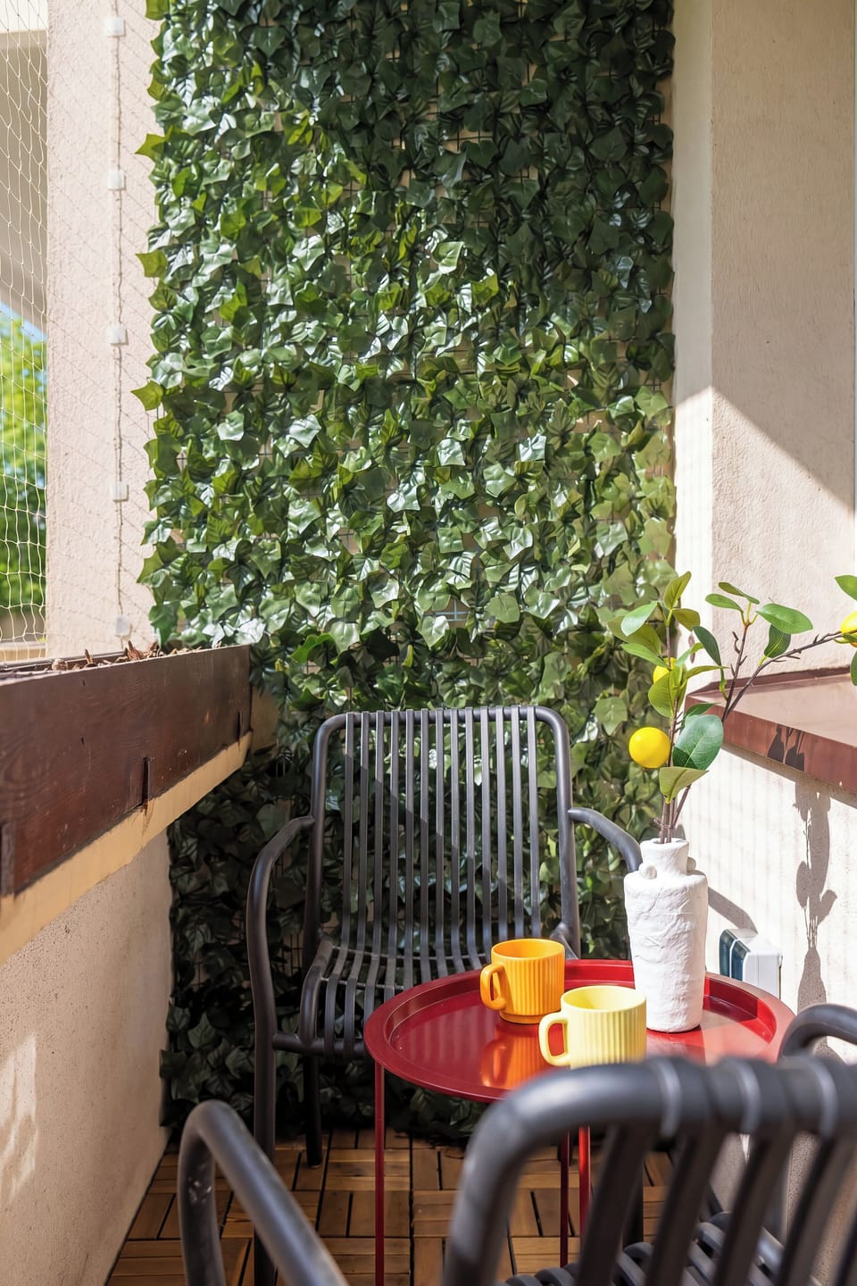 The balcony seating area features two dark wicker chairs and a small table set against a vibrant green backdrop. A bowl of fresh fruit on the table adds a pop of natural color to the scene.