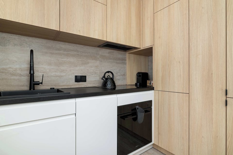 The kitchen workspace shows clean white cabinetry contrasted by a black countertop, sink, and faucet. Upper cabinets in a light wood grain finish provide ample storage above the sleek induction cooktop.