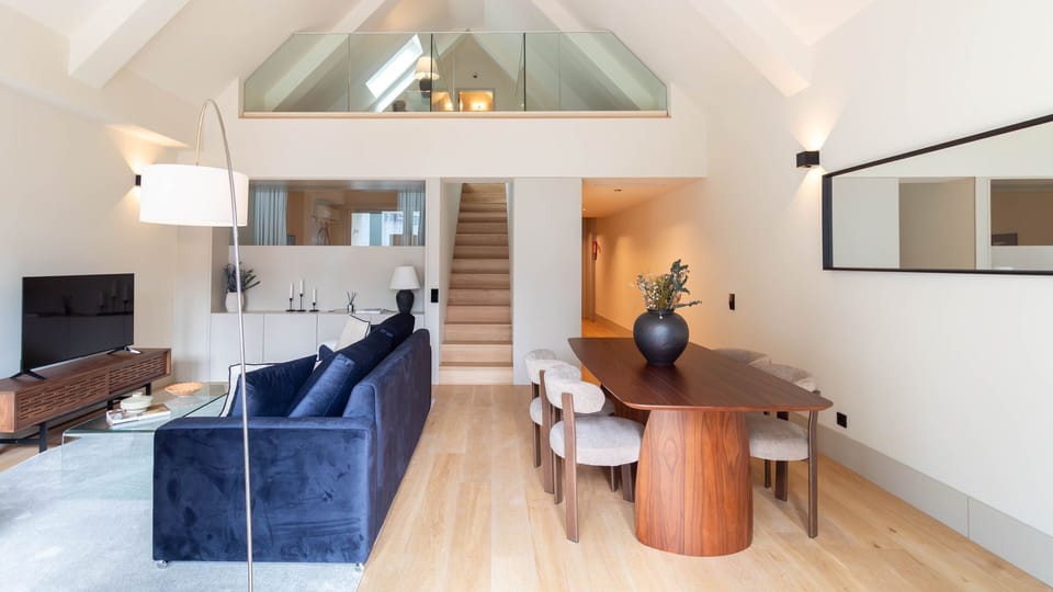 Spacious open-plan living and dining area with warm wooden finishes, high ceilings, and a charming mezzanine level. #Trendy #Gorgeous #LovelyStay