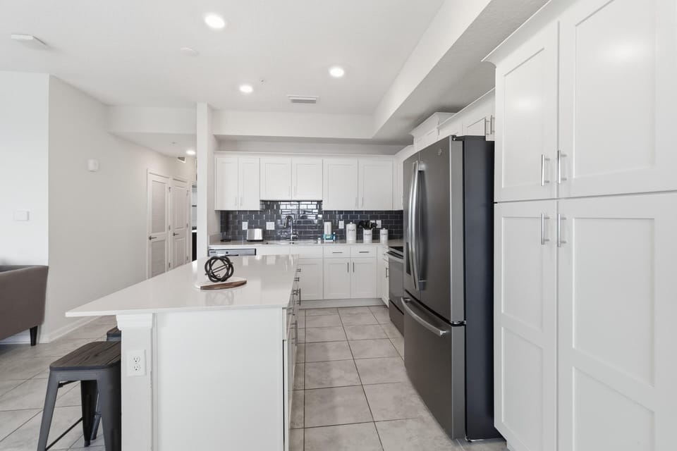 White shaker cabinets and a glossy dark tile backsplash frame the kitchen with stainless steel appliances.