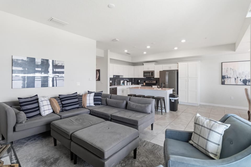 Open-concept living area with gray sectional, matching ottomans, blue armchair, and abstract wall art.
