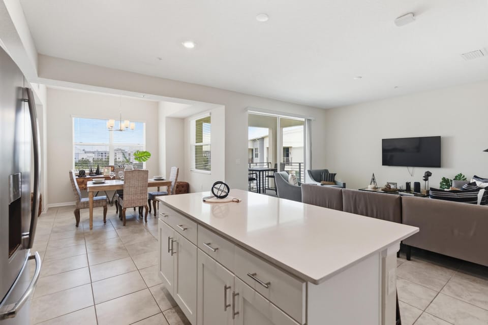 White quartz island separates the kitchen from the living room with a wall-mounted TV and sliding glass doors to the balcony.