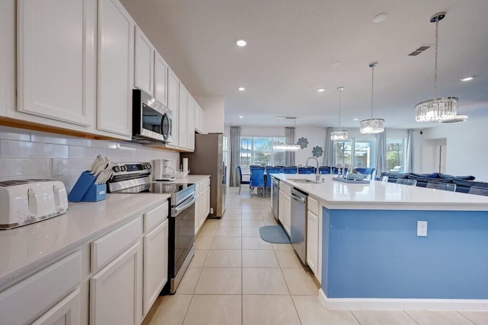 Fully equipped modern kitchen with white cabinetry, stainless steel appliances, and a large island with blue accents.