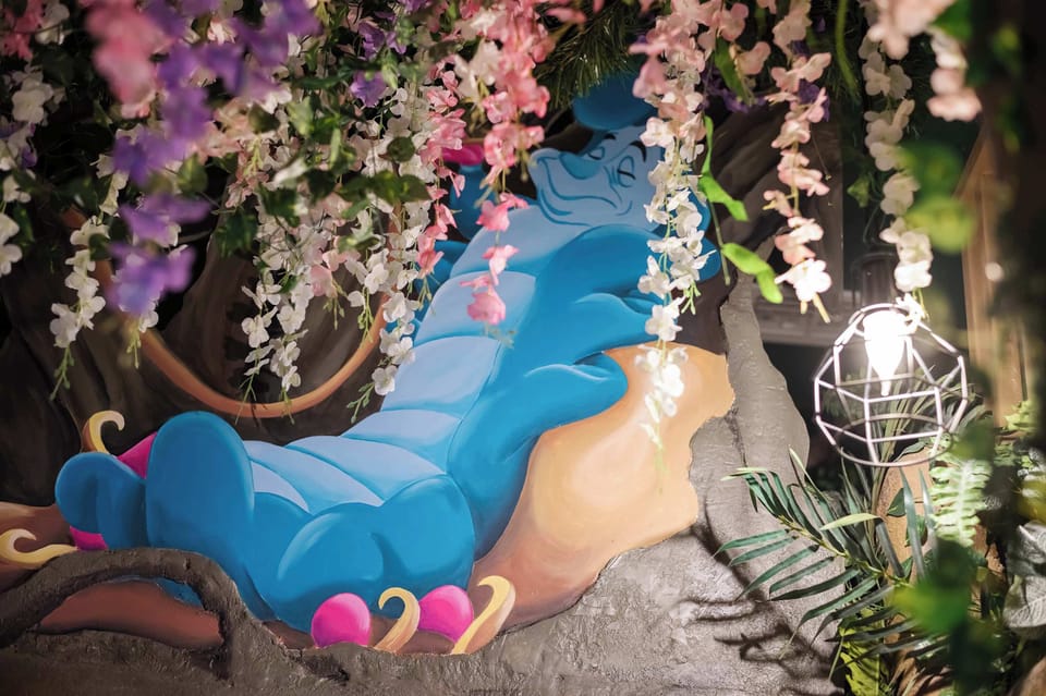 A whimsical blue caterpillar sculpture surrounded by hanging flowers and greenery.
