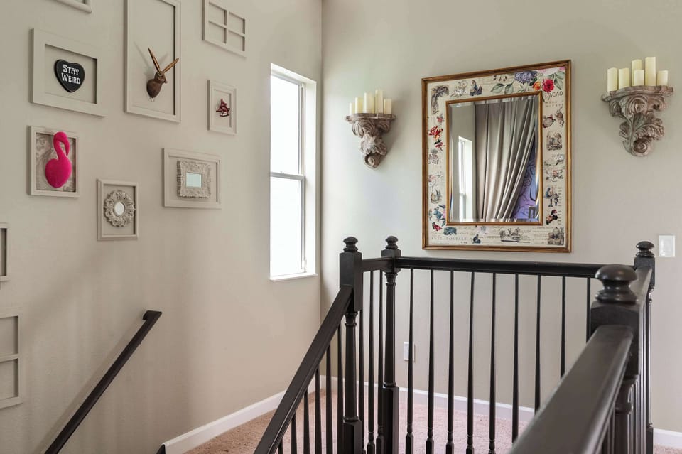 A stairwell with black railings, decorative wall art, and a large framed mirror with candle sconces.