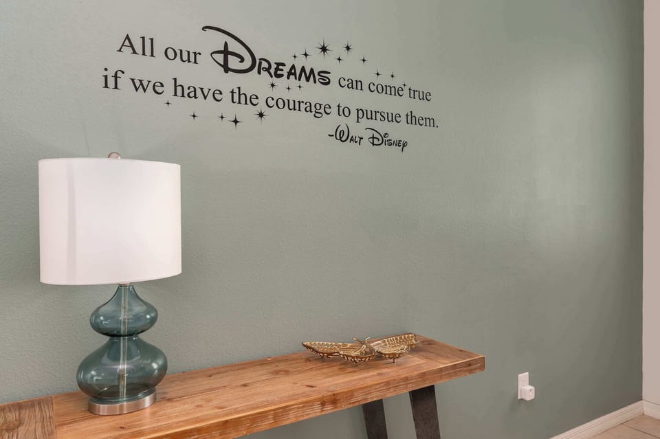 A wooden console table with decorative accents and a lamp beneath an inspirational wall quote.