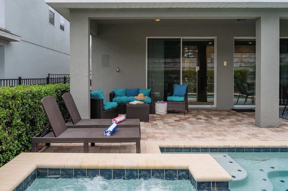 Covered patio with wicker seating and poolside loungers next to a bubbling spa.