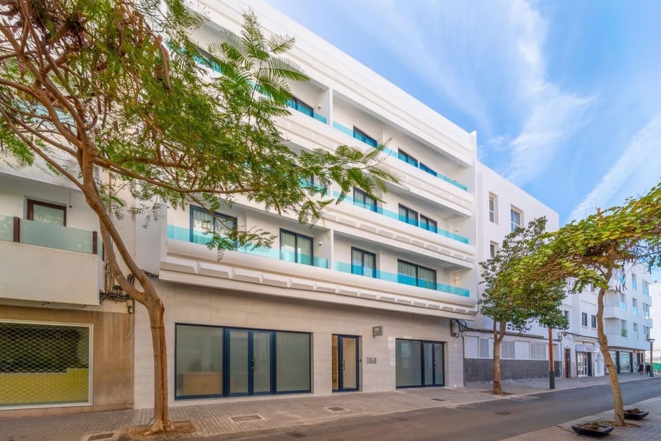 A modern white apartment building with stylish balconies on a sunny city street.