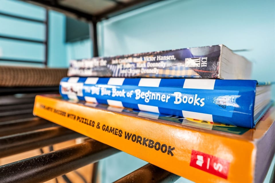 A small stack of books and workbooks on a metal shelf against a teal wall.