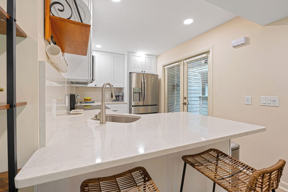Crisp white cabinetry, quartz countertops, stainless steel appliances, and a large breakfast bar create a bright, welcoming space.