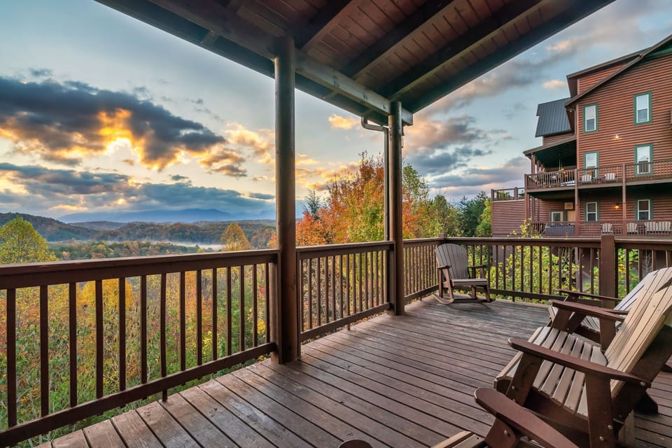 Covered wraparound deck with rocking chairs and breathtaking Smoky Mountain sunset views, perfect for relaxing outdoor seating and peaceful cabin stays.