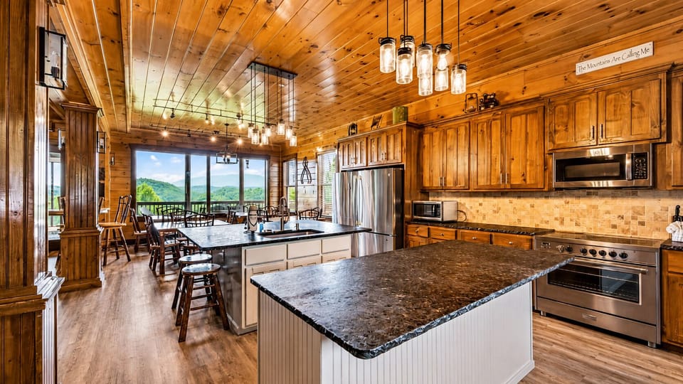 Fully equipped cabin kitchen with two granite islands, bar stools, stainless-steel refrigerator, microwave, extensive wood cabinetry, and generous meal-preparation space.