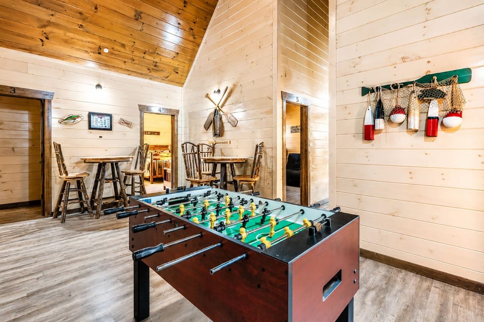 Foosball game room with two arcade cabinets, rustic bar tables, wood-plank walls, vaulted ceiling, and family-friendly indoor entertainment.