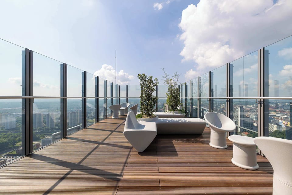 An expansive rooftop terrace features dark wooden decking, contemporary white outdoor lounge furniture, and glass safety railings. The open sky and clouds are visible, offering a panoramic viewpoint.