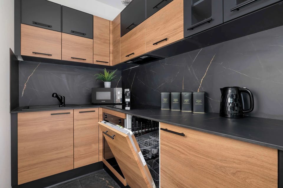 A detailed view of the kitchen shows the dishwasher door slightly open, revealing the integrated design. The craftsmanship of the wood grain and black hardware is clearly visible.