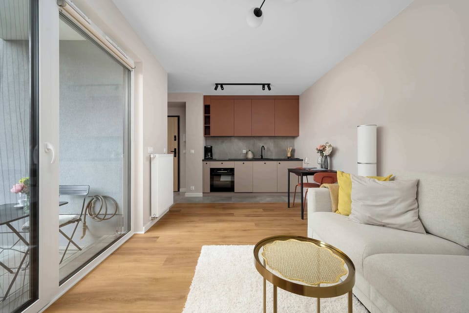 A wide-angle view reveals the open-plan layout connecting the living area to the kitchen in the background. The seamless integration of light wooden floors ties the entire living space together beautifully.