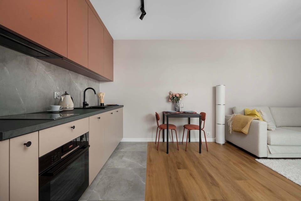 The kitchen workspace extends along the wall, showing ample counter space next to the open living room. Modern appliances are neatly integrated into the minimalist cabinet design.